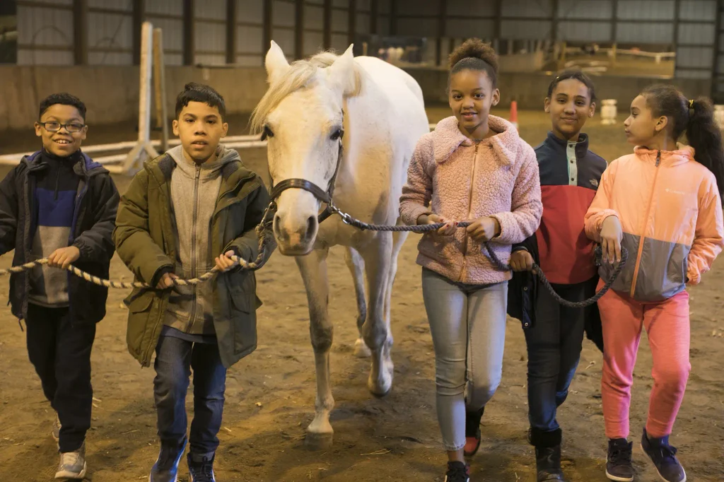 children leading a horse in a barn